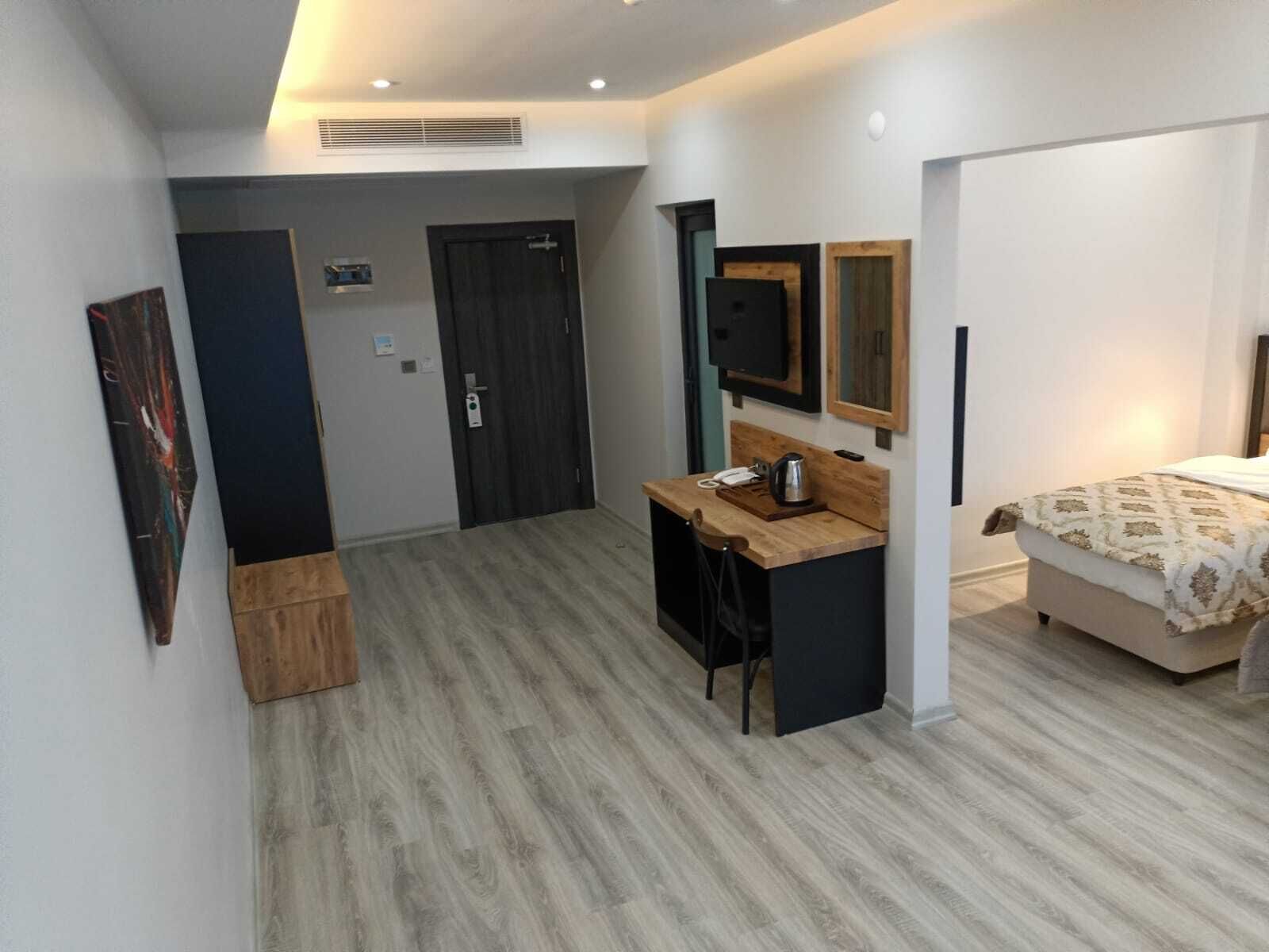 A modern hotel room with a wooden desk, a bed with patterned bedding, a TV mounted on the wall, and a small seating area.