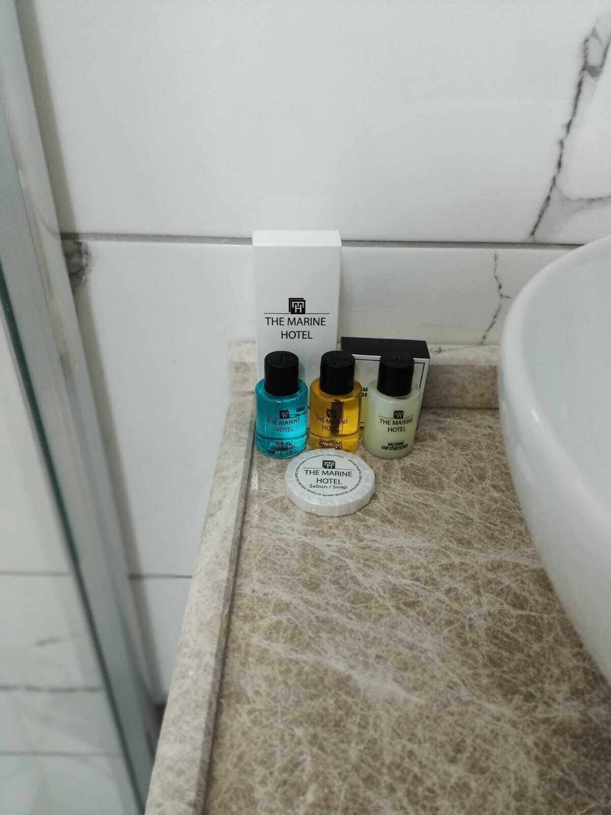 Una encimera de baño con tres botellas de champú y una barra de jabón con la etiqueta "The Marine Hotel".