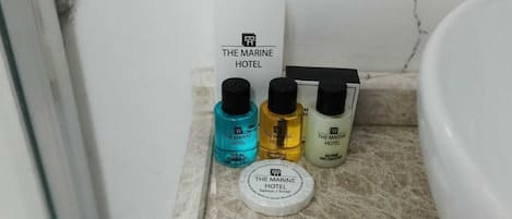 Una encimera de baño con tres botellas de champú y una barra de jabón con la etiqueta "The Marine Hotel".