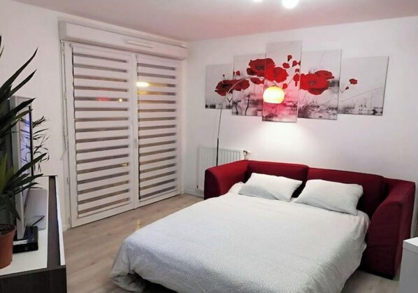 A bedroom with a bed, a red headboard, a wall-mounted light, and a sliding door.