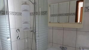 Ein Badezimmer mit einer gläsernen Duschkabine, einem weißen Waschbecken und einem Spiegel darüber.