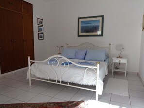 A bedroom with a bed, a nightstand, a lamp, a wardrobe, and a framed picture on the wall.