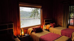 A room with two beds, a window with a view of a river and greenery, and a nightstand with a lamp. - Costa del Sol Iguazú Nature, river & Jacuzzi (Puerto Iguazú)
