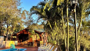A pool area with lounge chairs, a wooden building, and surrounding palm trees. - Costa del Sol Iguazú Nature, river & Jacuzzi (Puerto Iguazú)