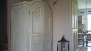 Un pasillo con un armario blanco grande, una mesita con una vela y un comedor al fondo.