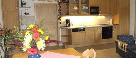 A kitchen with wooden cabinets, a microwave, and a coffee maker. There is a vase with flowers on the table.
