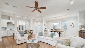A spacious living area with a white sofa, a coffee table, and a dining table in the background. - Great summer deals! Golf cart & bikes included! Steps to pool, close to beach (Santa Rosa Beach)