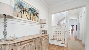 A hallway with a wooden cabinet, a lamp, and a painting of palm trees. - Great summer deals! Golf cart & bikes included! Steps to pool, close to beach (Santa Rosa Beach)