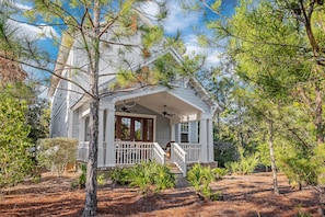 A two-story house with a porch, surrounded by pine trees and a well-maintained garden.