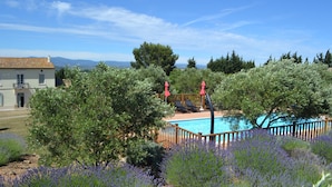 A pool area with a wooden deck, surrounded by lavender bushes, and a view of mountains in the background. - Canal View, superb gîte, Heated Pool near Carcassonne  next to Canal du Midi.  (Marseillette)