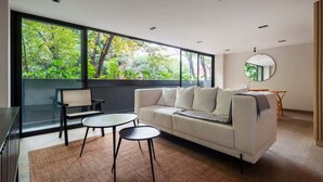 A modern living room with a large window, a sofa, two round tables, and a small round mirror. - w* | Outstanding 2BR with Balcony in Condesa (Ciudad de México)