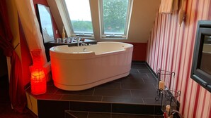 Ett modernt badrum med ett fristående badkar, två fönster, randig tapet och en ljusstake som lyser upp med rött sken.