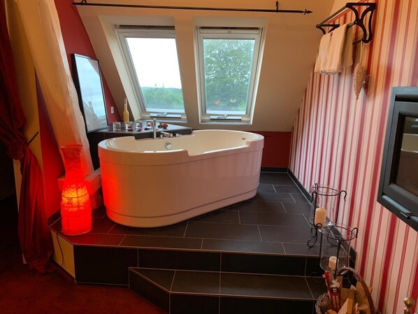 A modern bathroom with a freestanding bathtub, two windows, striped wallpaper, and a red-lit candle holder.