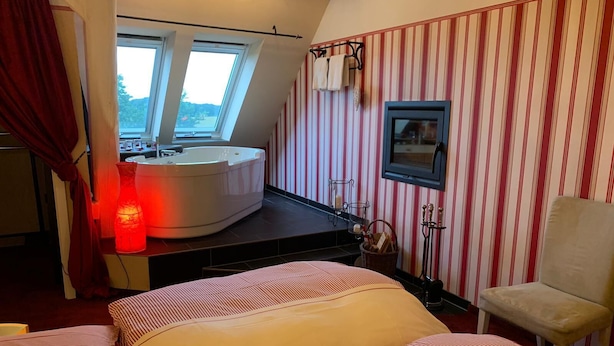 Ett hotellrum med en säng, ett badrum med badkar, ett fönster och randig tapet.