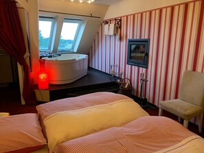 A hotel room with a bed, a bathroom with a bathtub, a window, and striped wallpaper.