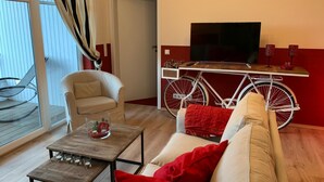 Ett vardagsrum med en soffa, ett soffbord, en tv på ett tv-bord, en cykel och en balkong med en stol.