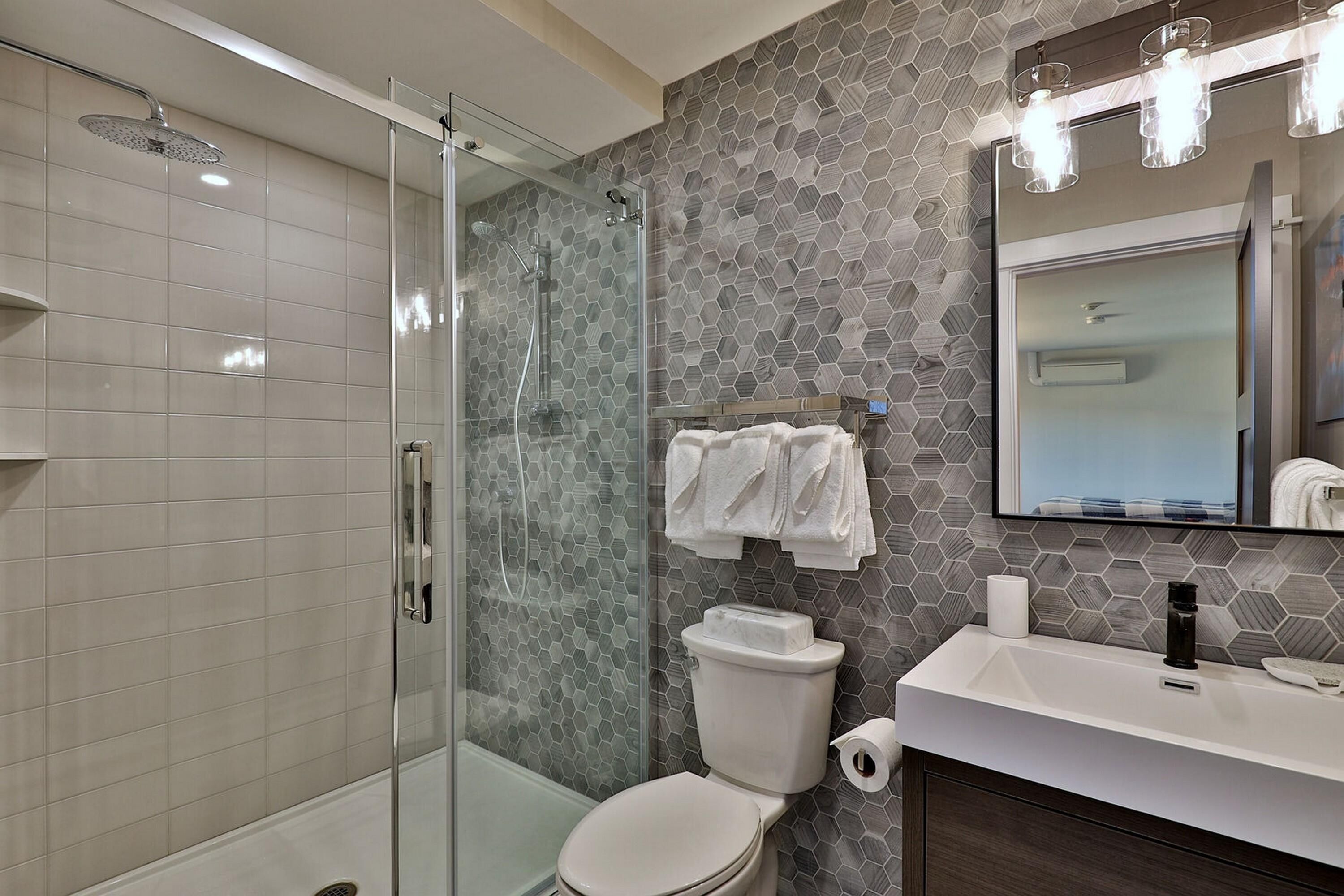 A bathroom with a glass shower enclosure, a toilet with a white lid, and a sink with a mirror above it.