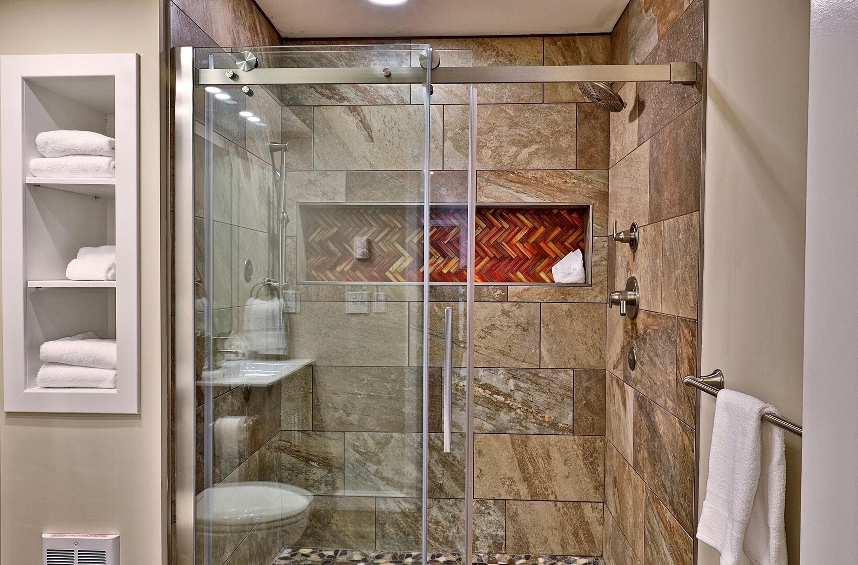 Un baño moderno con ducha de vidrio, azulejos de mármol y un estante empotrado con toallas.
