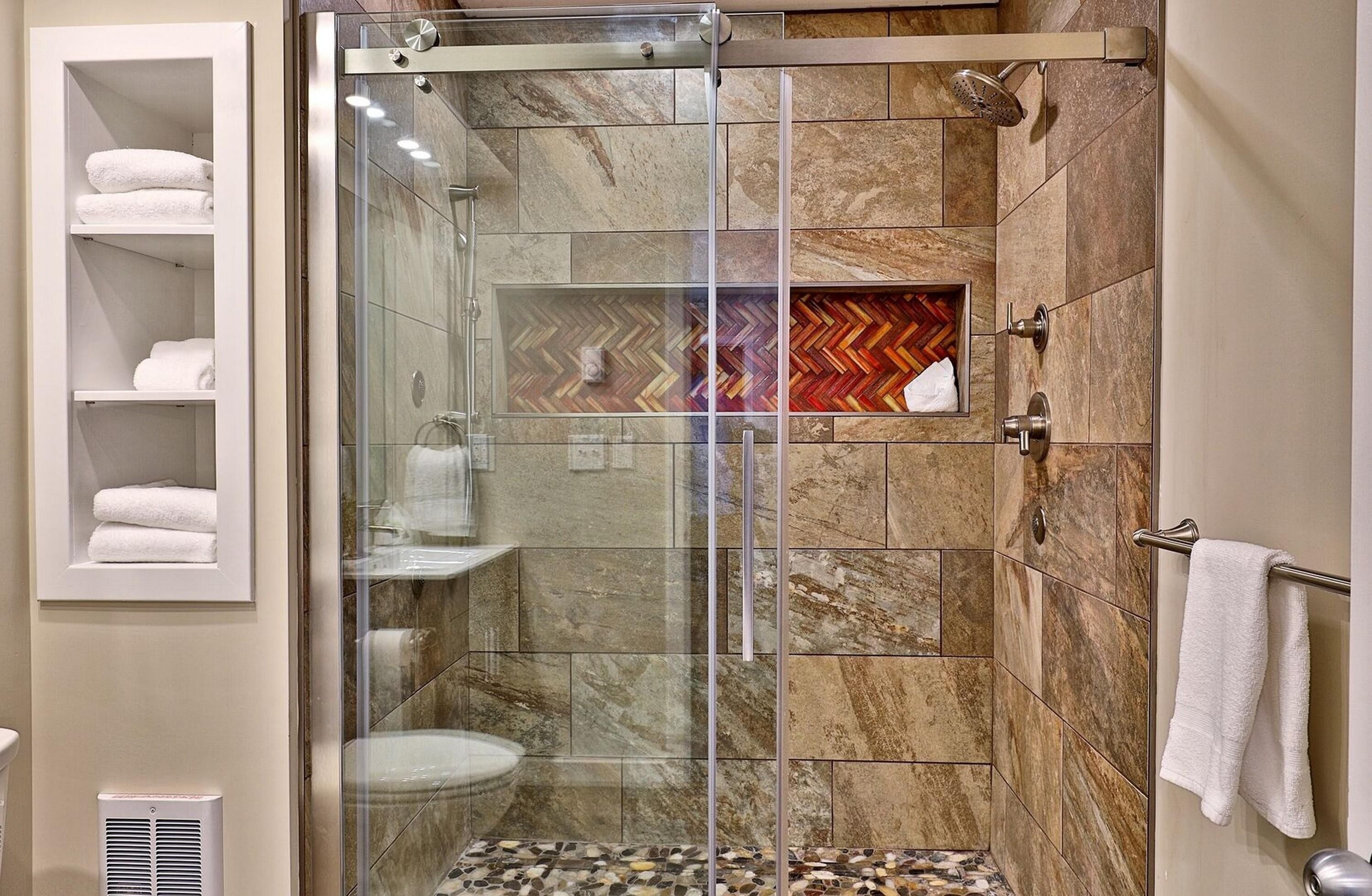 A modern bathroom with a glass-enclosed shower, marble tiles, a herringbone-patterned accent wall, and a towel rack.