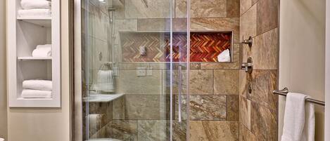 A modern bathroom with a glass-enclosed shower, marble tiles, a herringbone-patterned accent wall, and a towel rack.