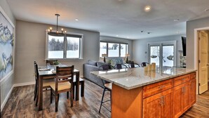 A modern kitchen with a central island, wooden cabinets, and a dining area with a table and chairs. - Killington Center Inn & Suites by Killington VR - 1 Bedrooms (Killington)