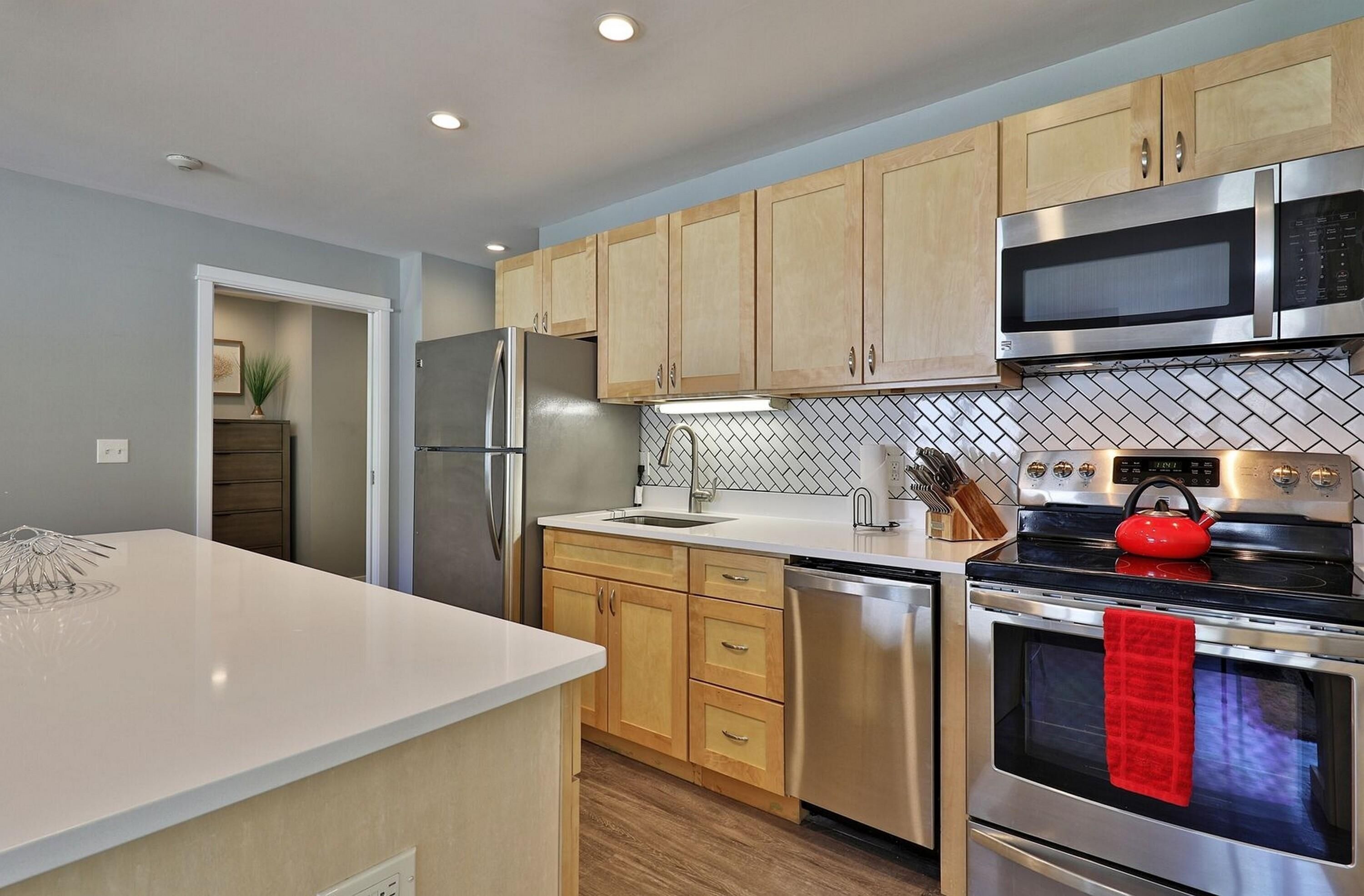 A modern kitchen with wooden cabinets, stainless steel appliances, and a tiled backsplash.