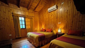 Une chambre de style cabane en bois, avec deux lits, une fenêtre avec des rideaux, un appareil de climatisation et un plancher en bois.