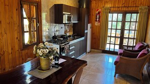 Un interior de madera con cocina, comedor y una silla de mimbre.