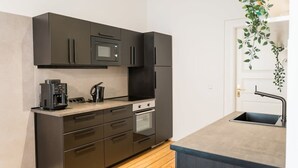 Une cuisine de taille réduite, dotée de meubles de rangement sombres, d’un four à micro-ondes, d’une machine à café et d’un évier.