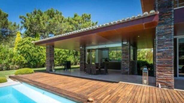 Ein modernes Haus mit einer Holzterrasse, einem Swimmingpool und einem überdachten Außenbereich mit Grill.