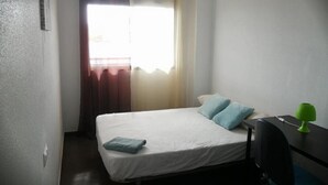 Una habitación pequeña con cama individual, escritorio y silla.