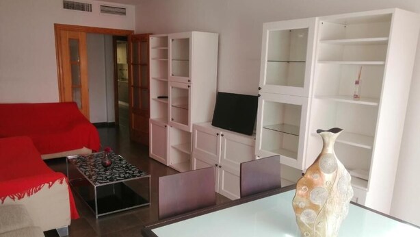 Una sala de estar con un sofá rojo, una mesa de centro, un televisor y un jarrón decorativo.