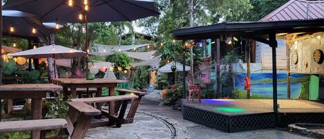 Een terras buiten met houten tafels en parasols, omgeven door groen.