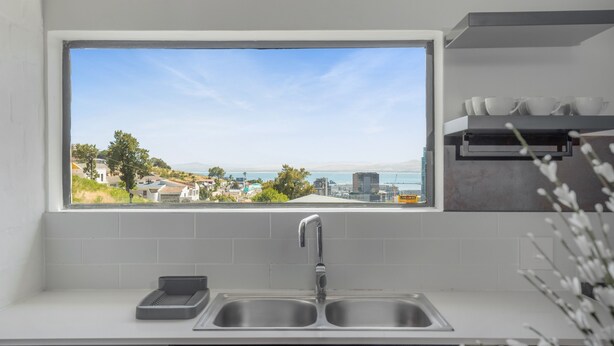 A kitchen with a large window overlooking a coastal town, a double sink, and a shelf with cups and bowls. - Contemporary 3-Bedroom in Bo-Kaap | Views and Pool (Cape Town)