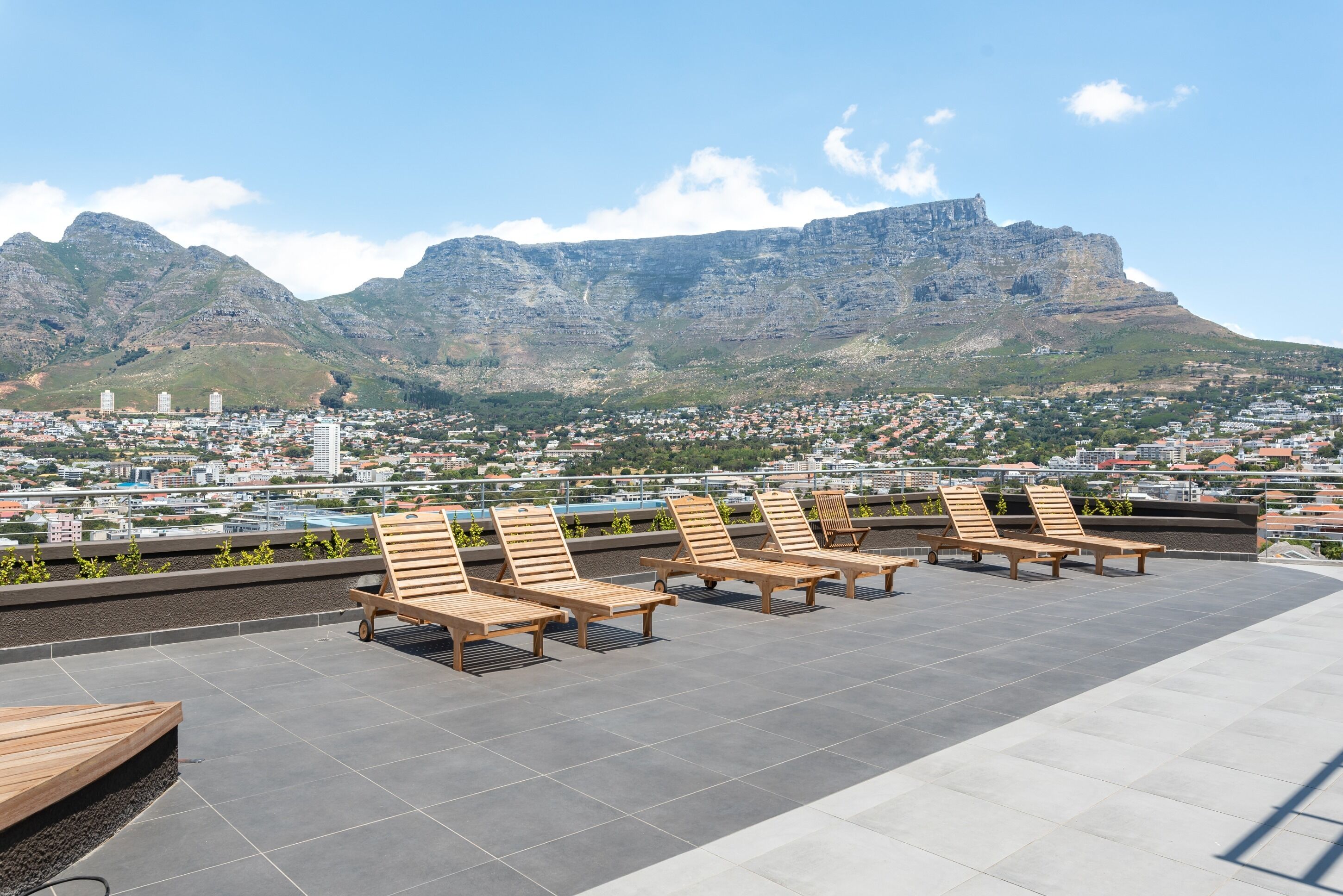 A rooftop terrace with wooden loungers and a cityscape view.