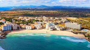 A coastal town with a beach, buildings, and mountains in the background. - Mix Peymar (Sant Llorenc des Cardassar)