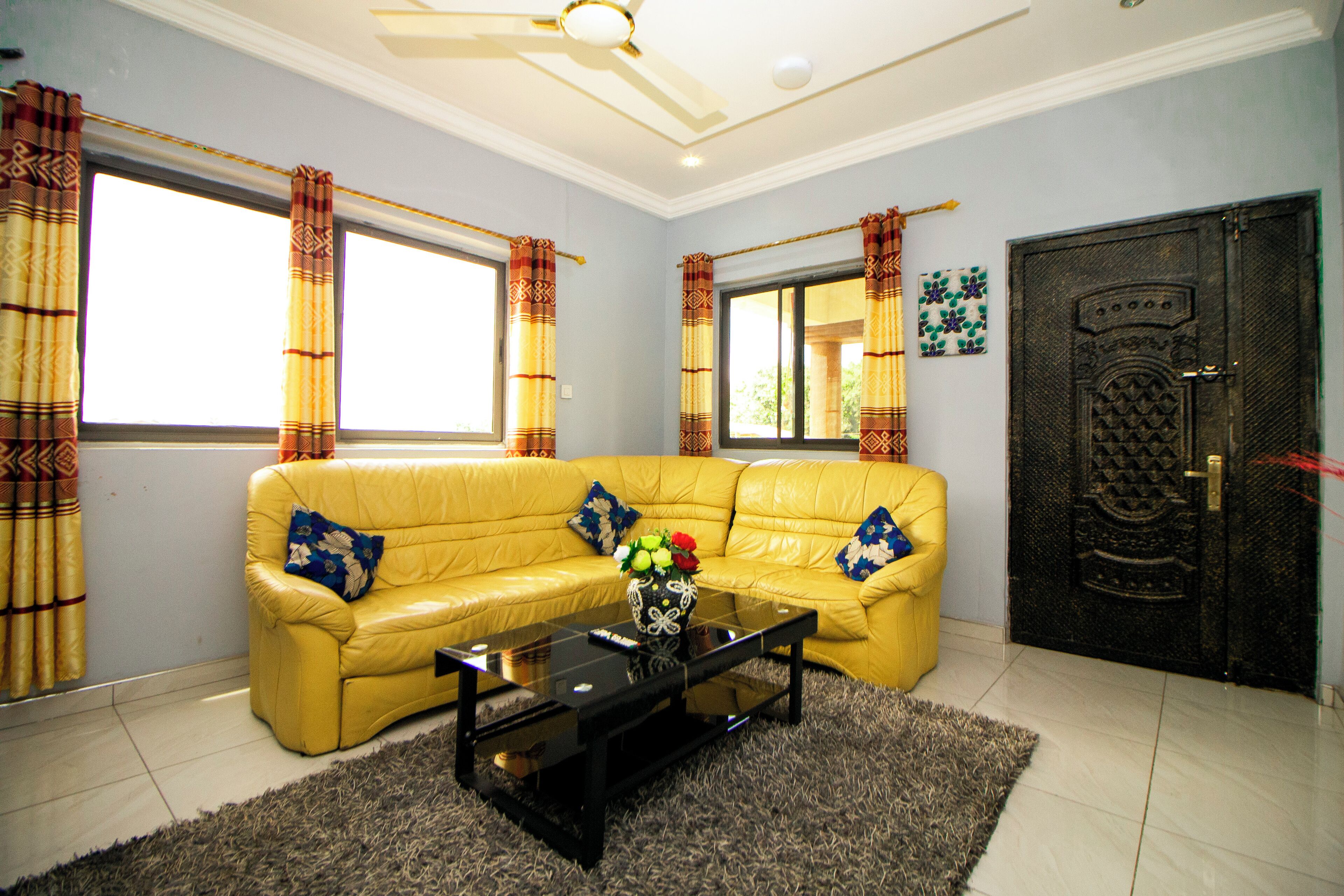 A living room with a yellow sofa, a glass coffee table, and a decorative vase.