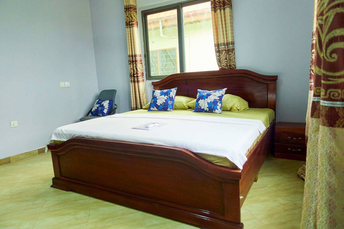 A bedroom with a wooden bed, two pillows, a nightstand, and a window with curtains.
