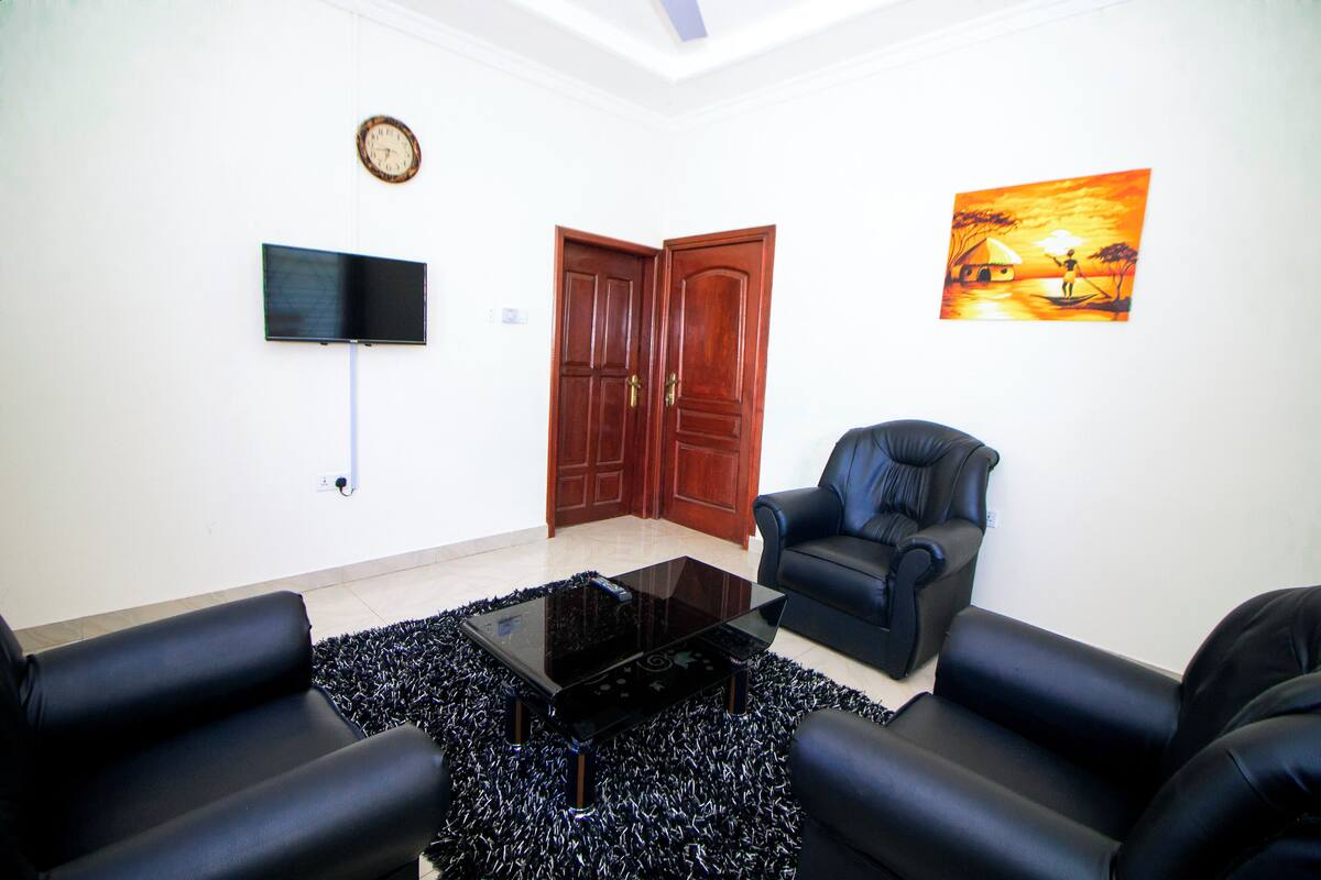 A living room with a flat-screen TV, a painting, a wooden door, and black leather sofas.