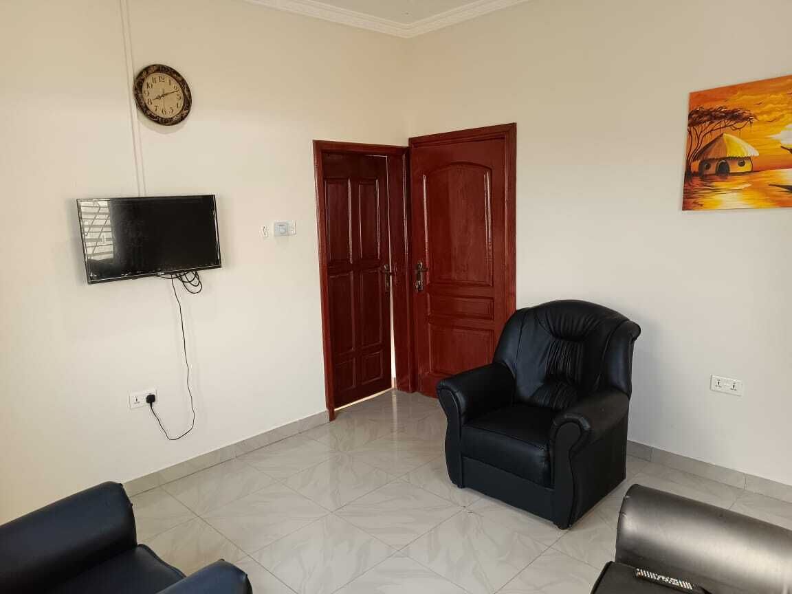 A room with a flat-screen TV mounted on the wall, a wooden door, a black leather chair, and a painting on the wall.