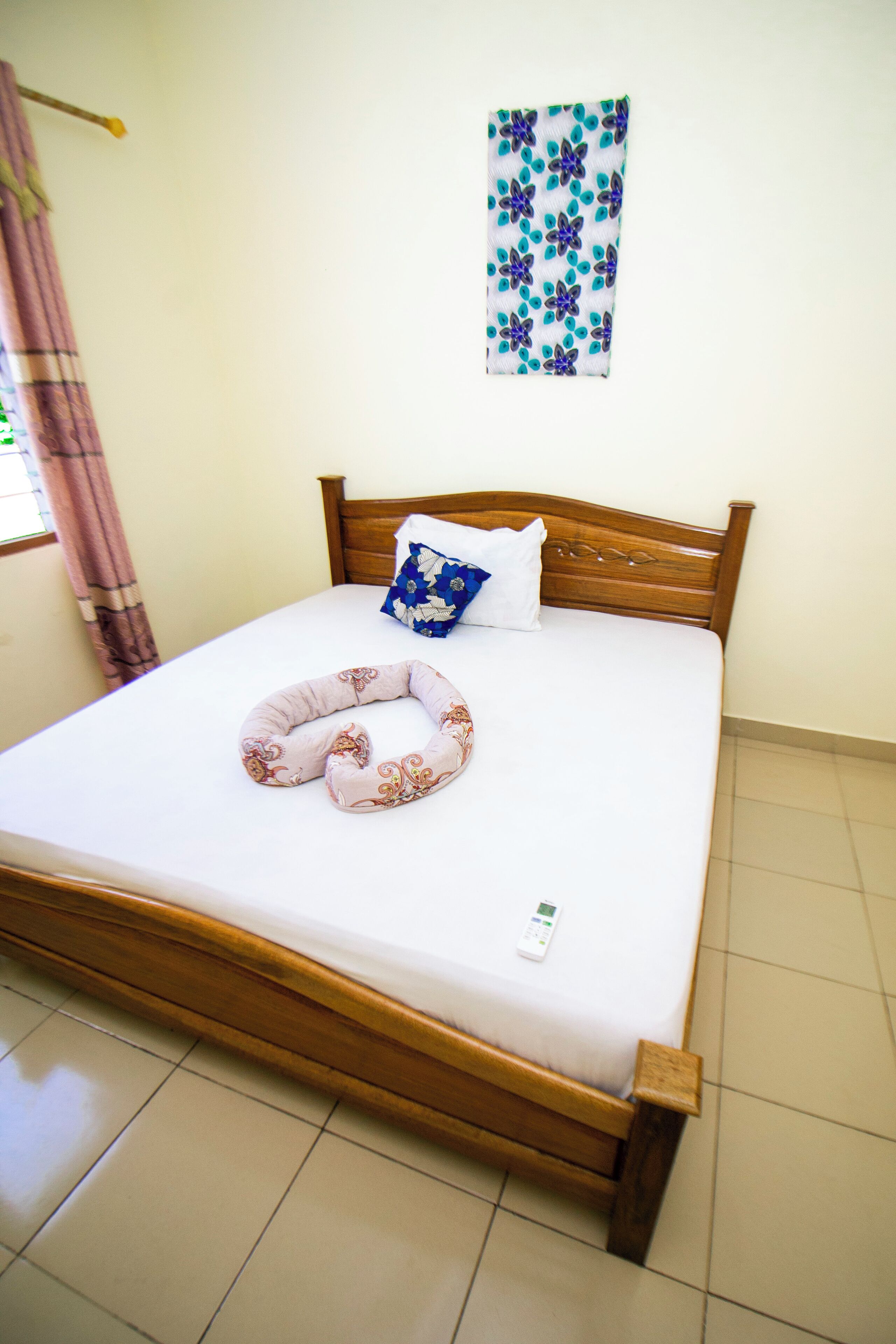 A neatly made bed with a pillow, a decorative pillow, and a remote control on the mattress.