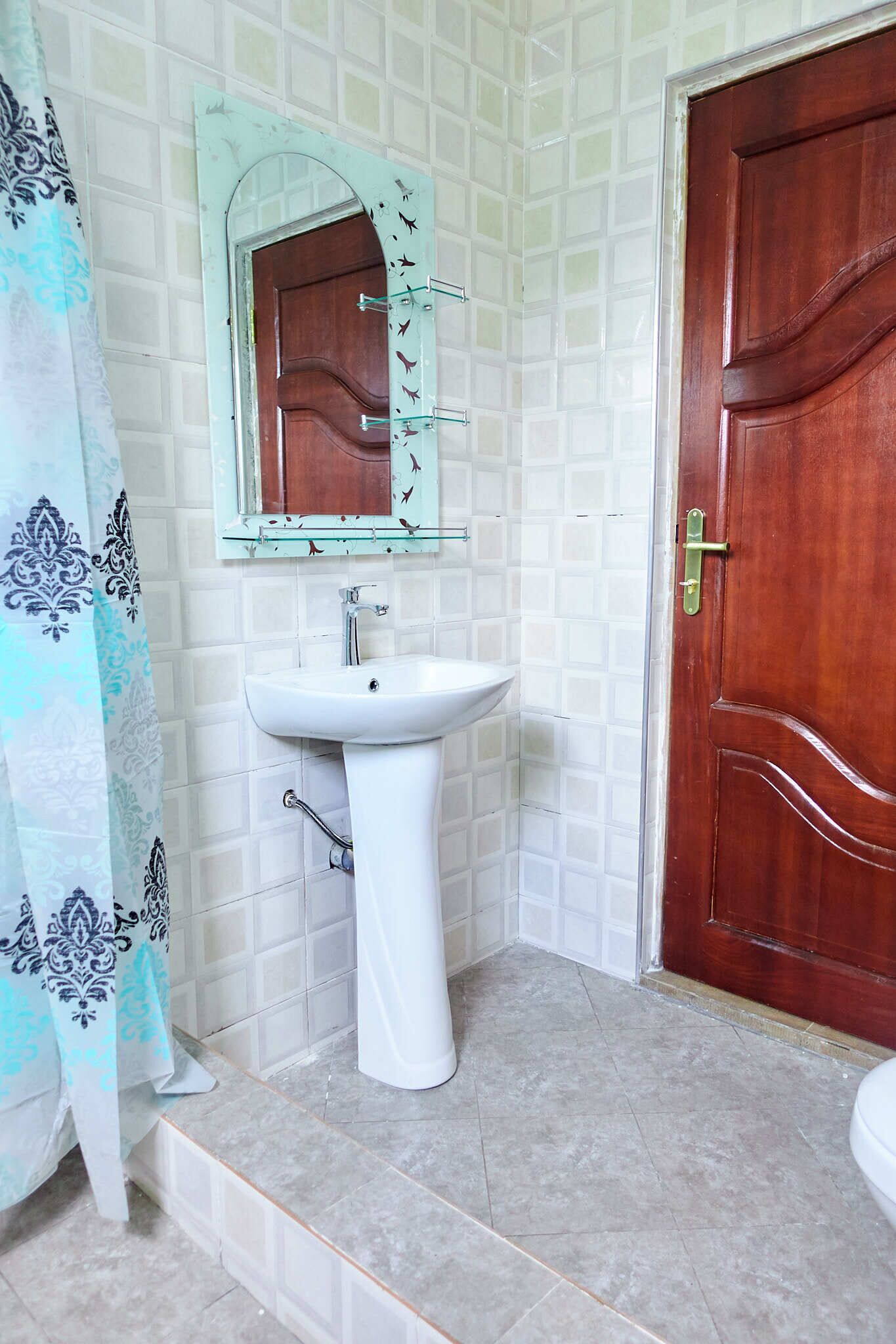 A bathroom with a white sink, a wooden door, and a patterned shower curtain.