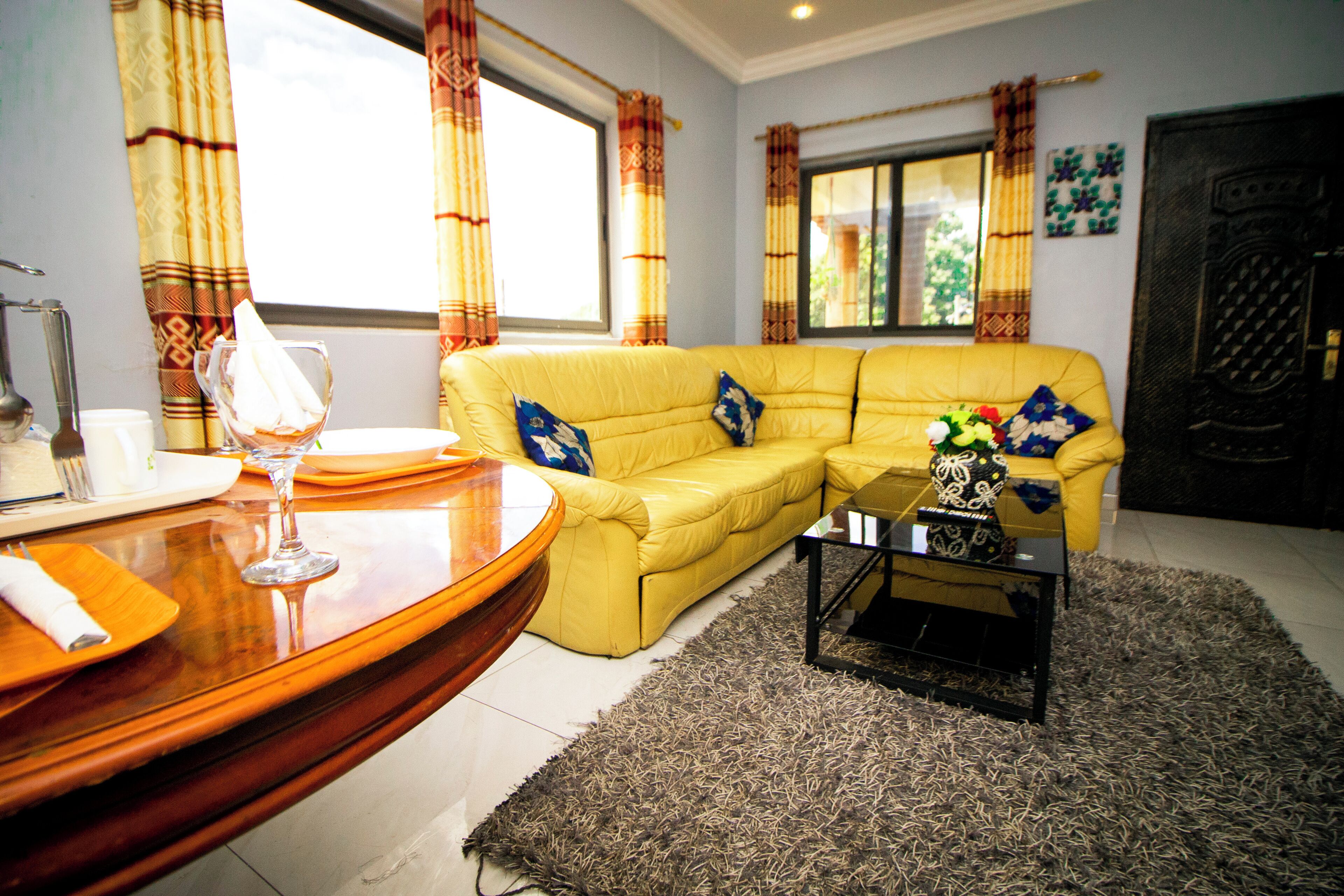 A living room with a yellow sofa, a glass coffee table, and a patterned rug.
