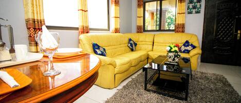 A living room with a yellow sofa, a glass coffee table, and a patterned rug.