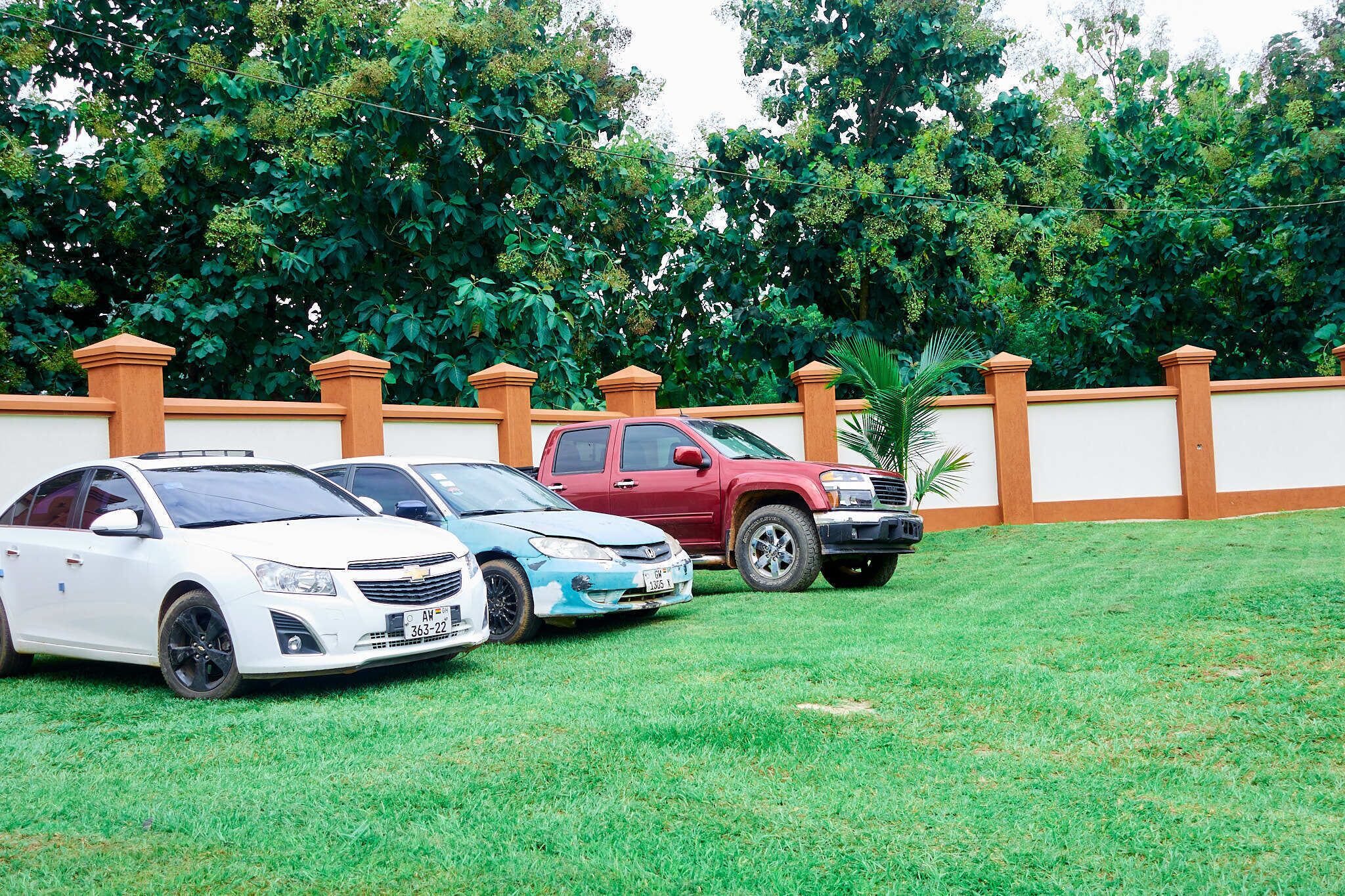 A parking area with three cars parked in front of a white wall with brown pillars.