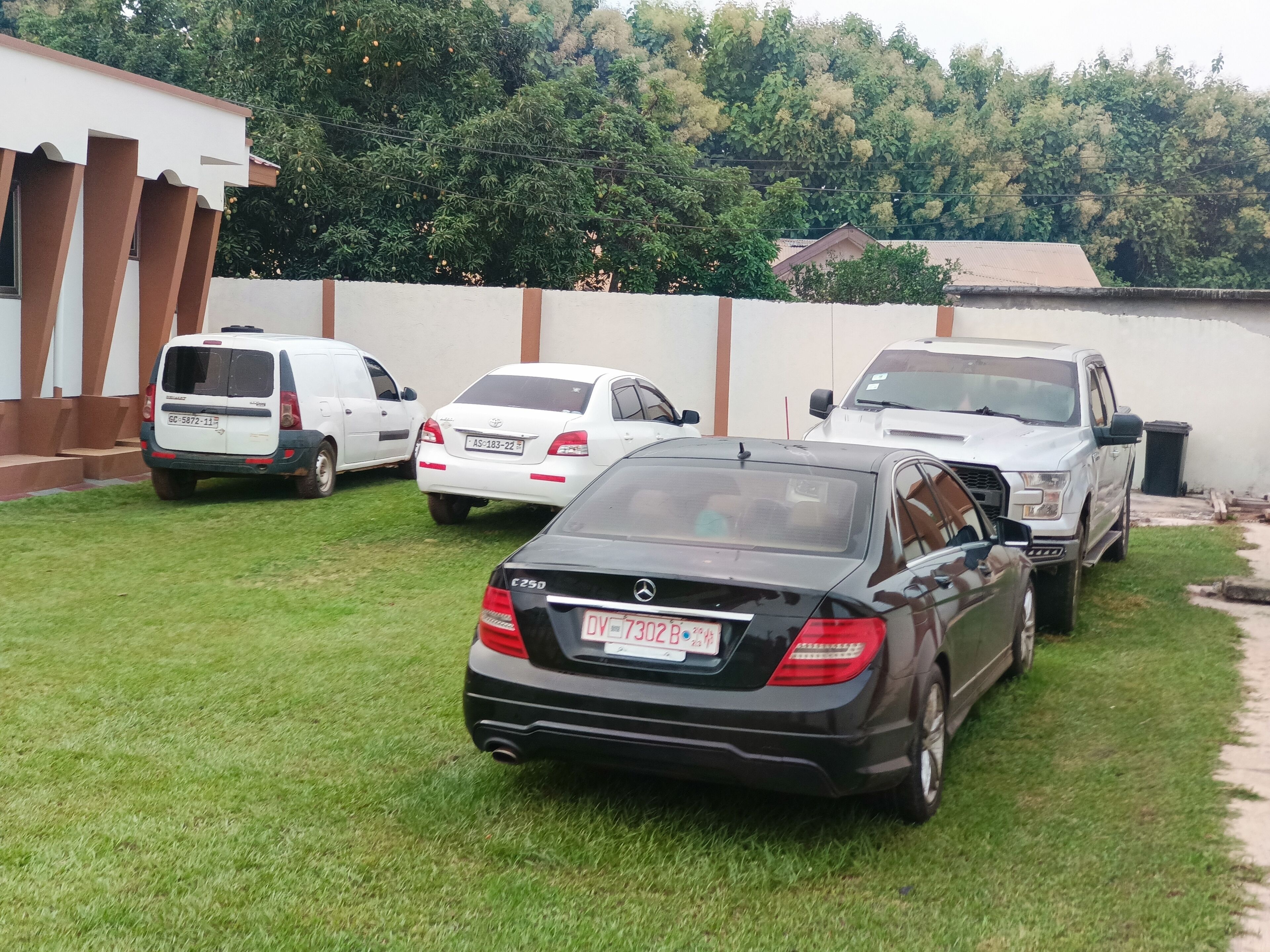 A parking area with several vehicles, including a white van, a white sedan, and a black sedan.