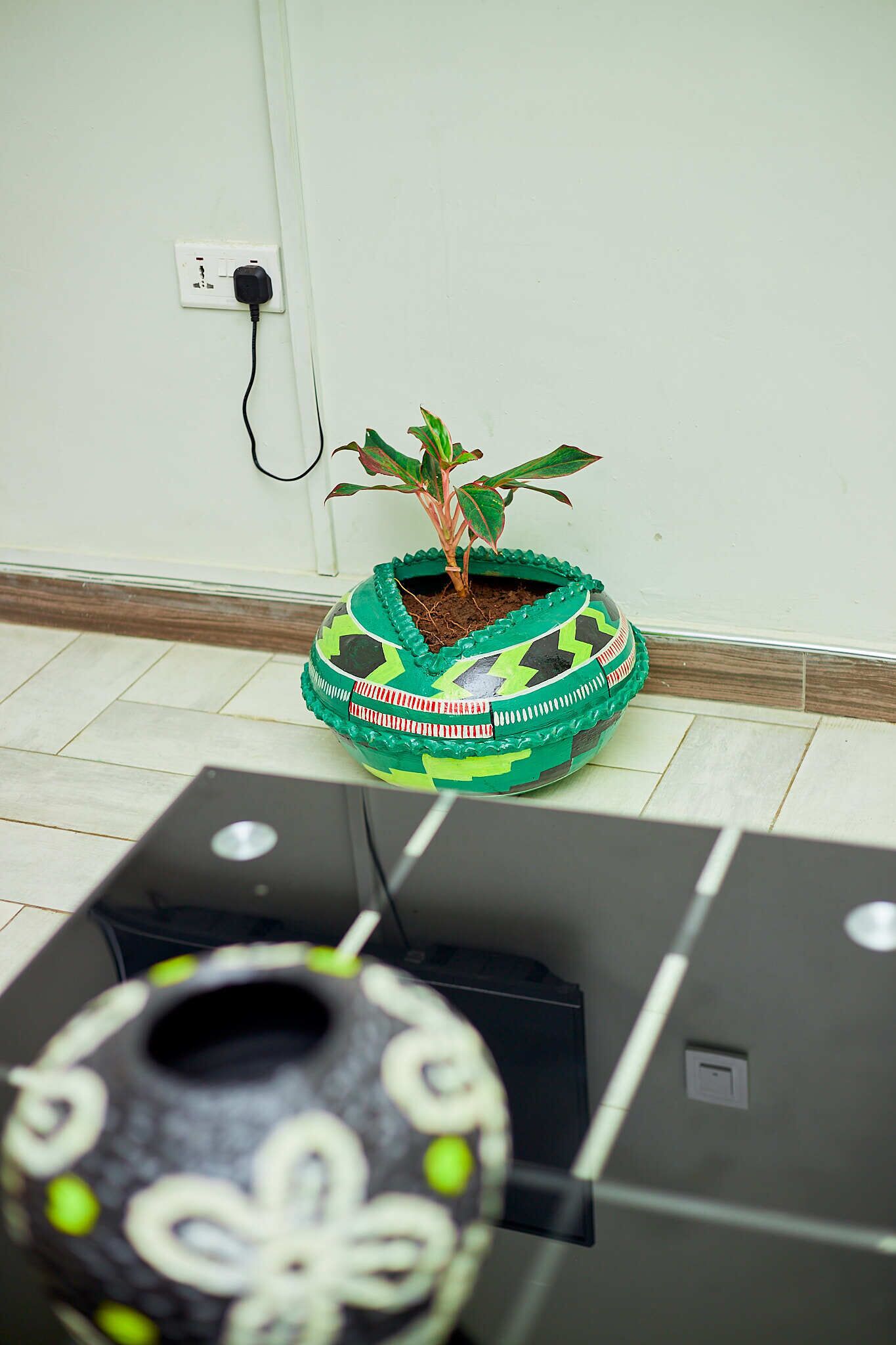 A potted plant on a tiled floor next to a black electronic device.