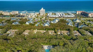 Vista aérea de una zona residencial costera con casas, una gran piscina y un hotel al fondo.