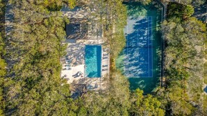 Vista aérea de una propiedad con piscina, cancha de tenis y árboles circundantes.