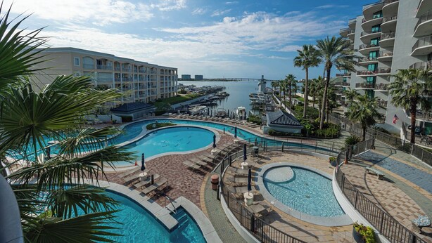 A resort with multiple swimming pools, palm trees, and a marina in the background.